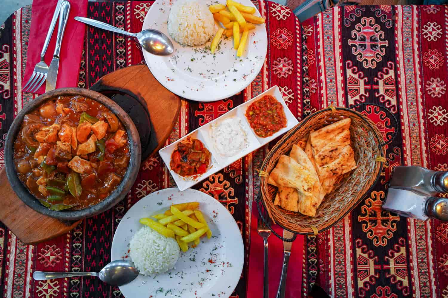 Turkish testi kebab on table with sides of rice, fries, pita bread, dips