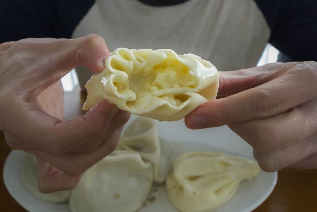 Person holding open cheese khinkali showing white cheese on the inside