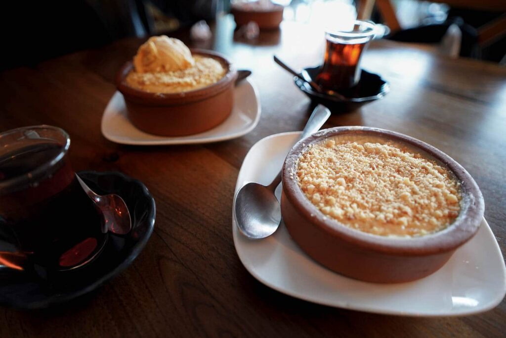 Two bowls of Turkish sütlaç with hazelnuts, ice cream and two glasses of tea