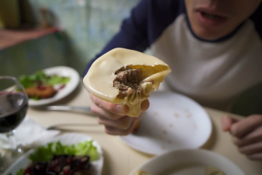 Man holding half eaten khinkali with meat inside visible