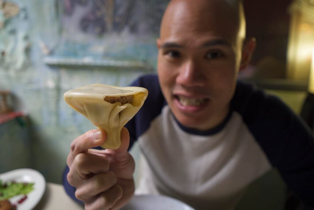 Man holding Georgian soup dumpling upside down with bite out of it showing meat inside