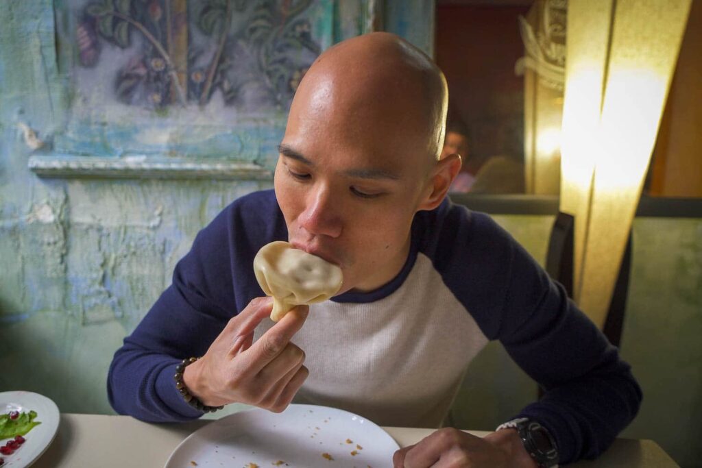 Man (Chris) nibbling side of Georgian soup dumpling to suck out soup