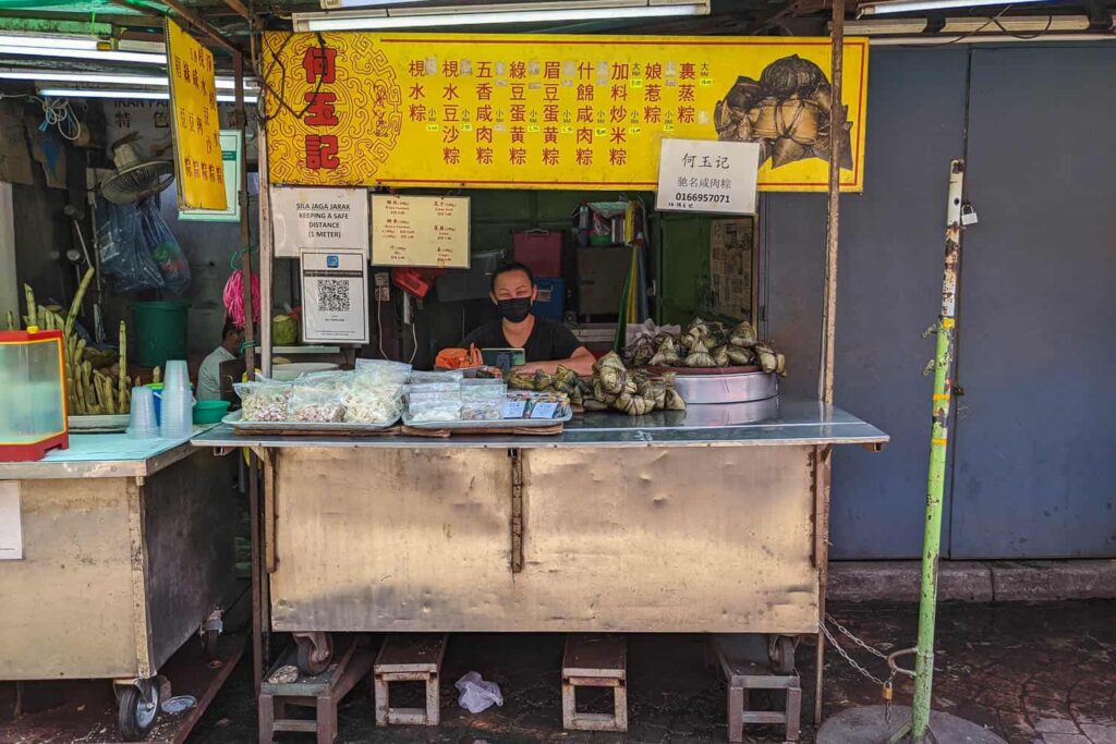 Lady sitting at Ho Yoke Kee joong metal hawker cart with yellow sign on Petaling Street Chinatown