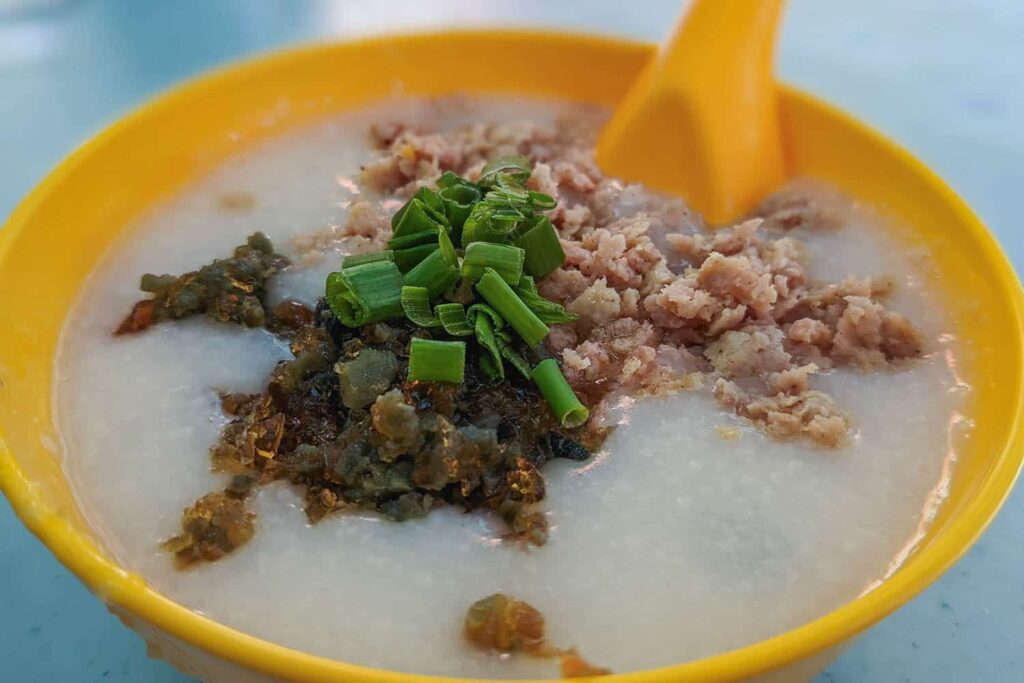 Yellow bowl of white rice porridge congee with century egg, pork and green onion on top