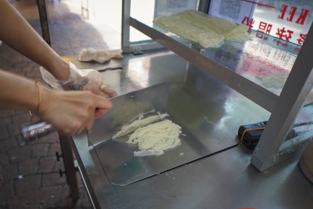 Woman chopping up chee cheong fun noodles with cleaver on metal cart