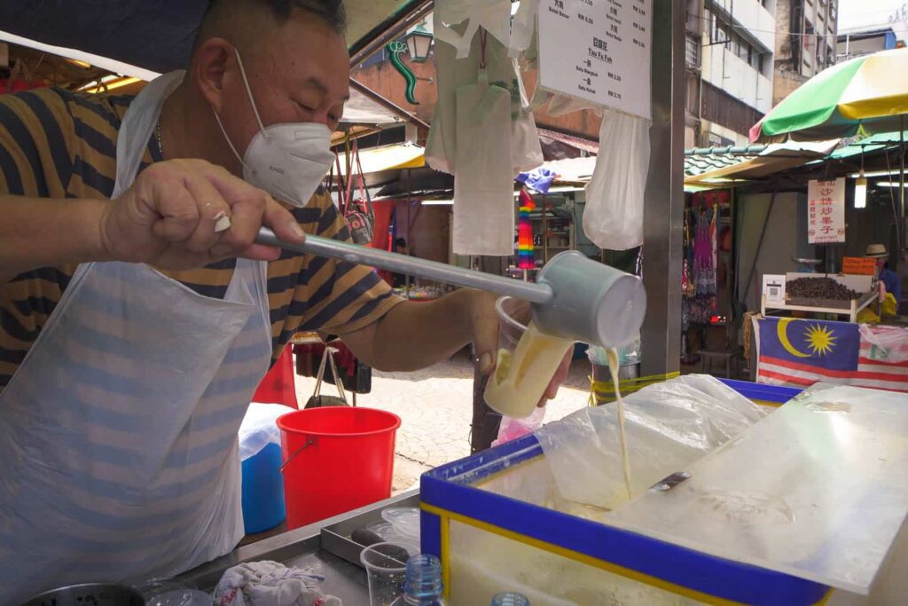 Man ladling soy bean drink into plastic cup on Petaling Street Chinatown
