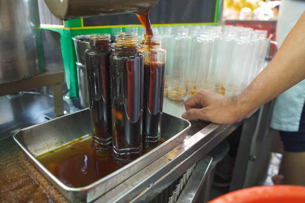 Dark brown liquid mata kucing filling four tall plastic bottles with many more empty behind