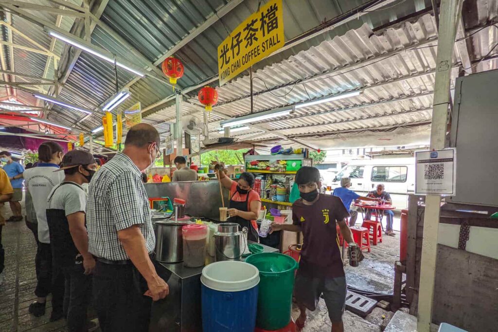 Drink hawker stall with woman pulling teh tarik, customers waiting in front