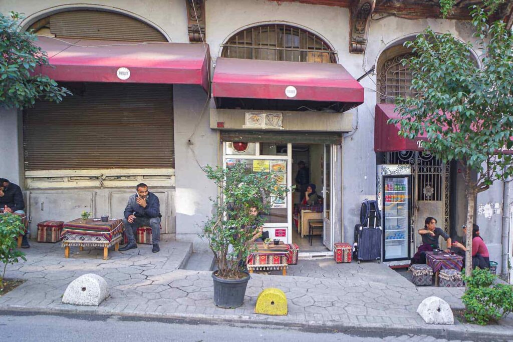 People sitting at small tables on side of road drinking Turkish tea and coffee