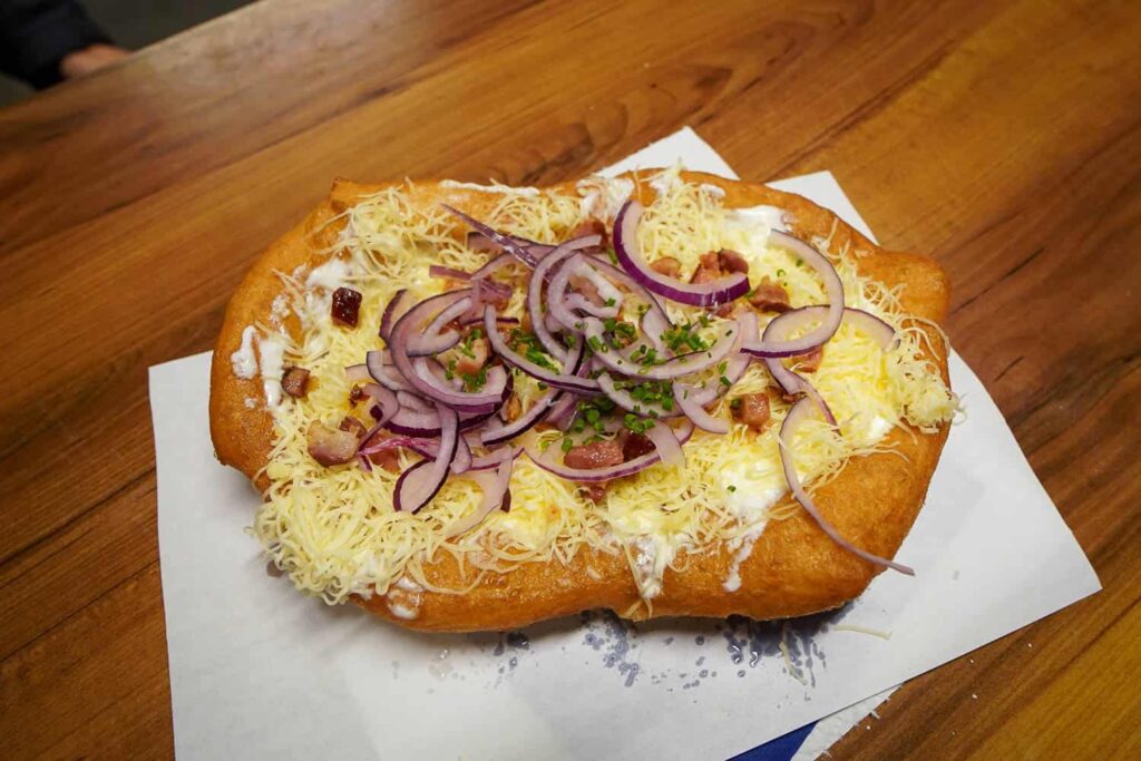 Langos covered in sour cream, cheese, bacon, onion