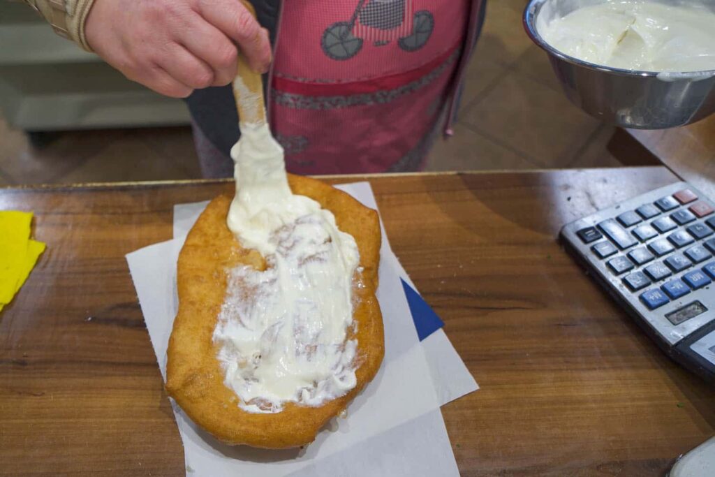 Woman spreading sour cream on the best langos in Budapest