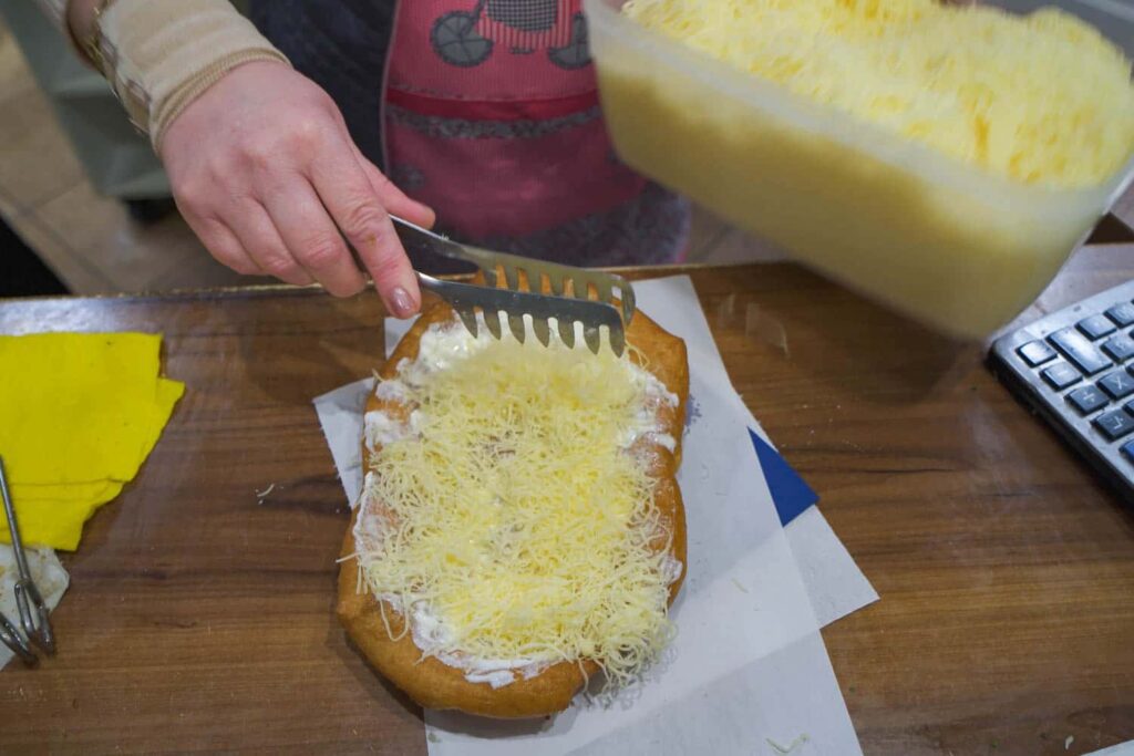 Woman putting cheese on sour cream and garlic langos