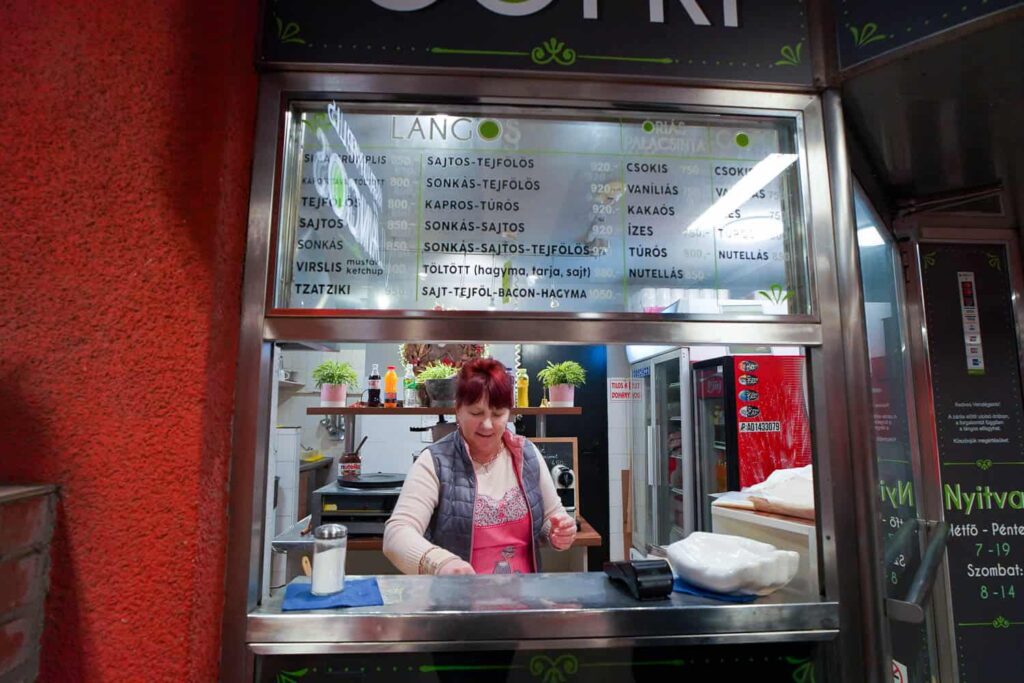 Woman selling langos with menu above at Krumplis Langos best langos in Budapest