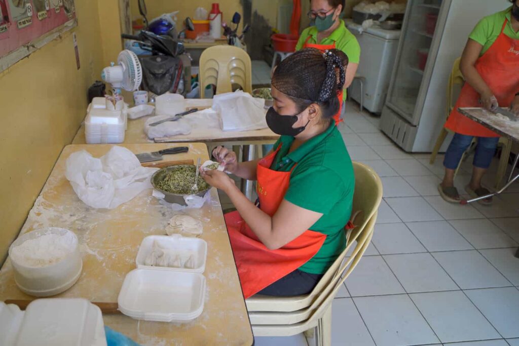 Woman sitting at table stuffing pork and chives into dumpling skin