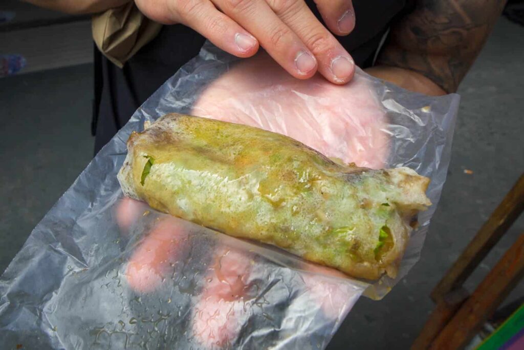 Hand holding fresh lumpia in plastic wrapper street in Quiapo Market