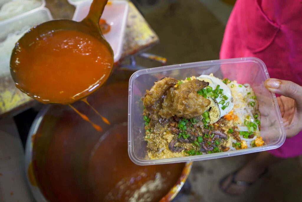 Ladle of palobok sauce spooning onto pancit noodles with chicharon and egg in container