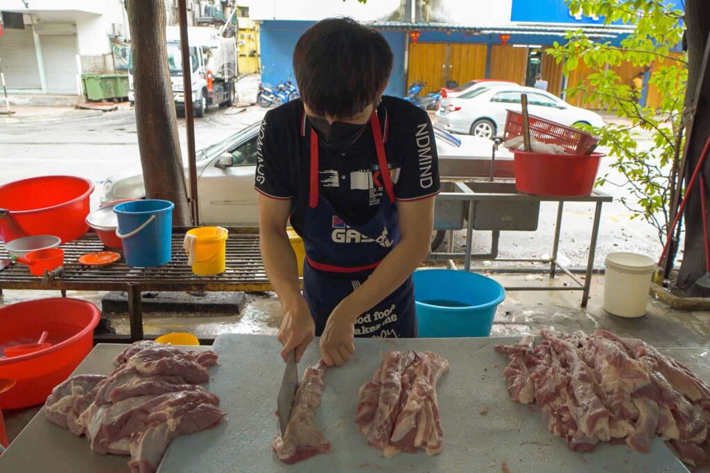 Man cutting strips of pork shoulder outside on table
