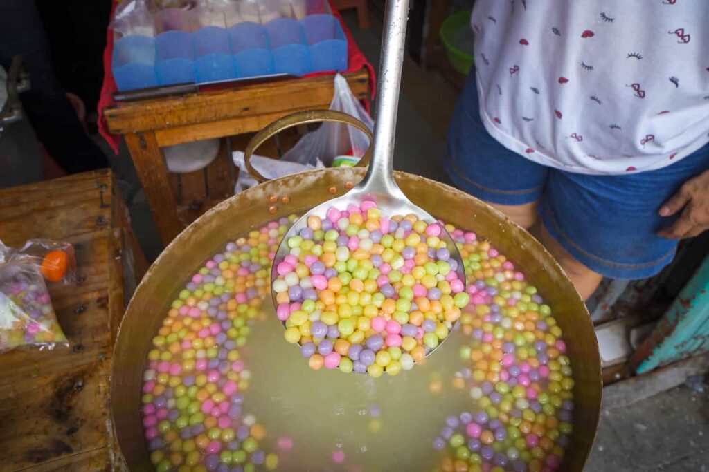 Ladle of colourful bua loy balls held above large pot