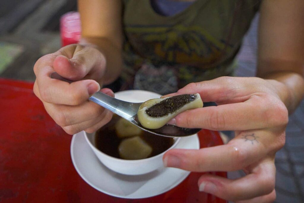 Glutinous black sesame ball being squeezed by two hands on spoon