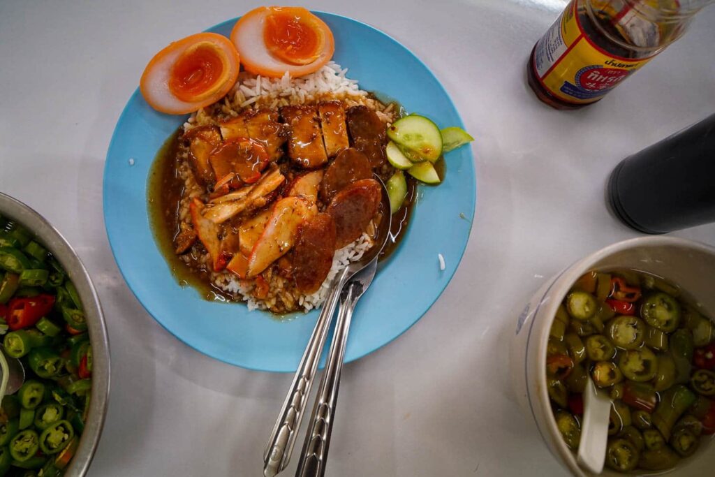 Plate of crispy and bbq pork on bed of rice covered in savoury sauce