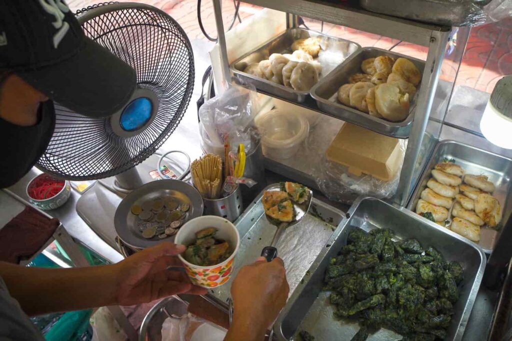 Man at hawker stall spooning gui chai tod into paper bowl