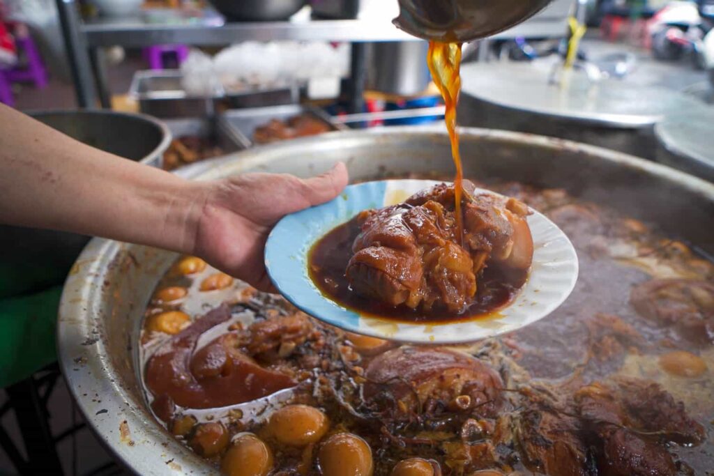 plate with marinated pork knuckle with ladle of sauce pouring overtop