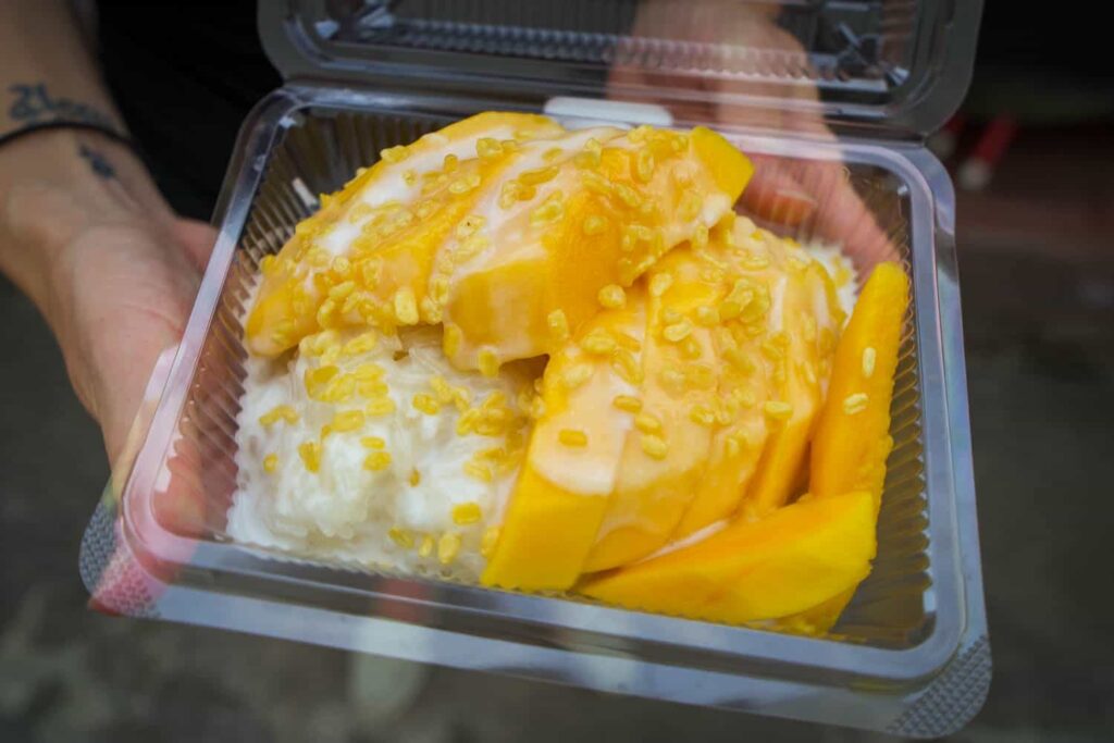 Plastic container of sticky rice with cut up mango on top covered in coconut cream