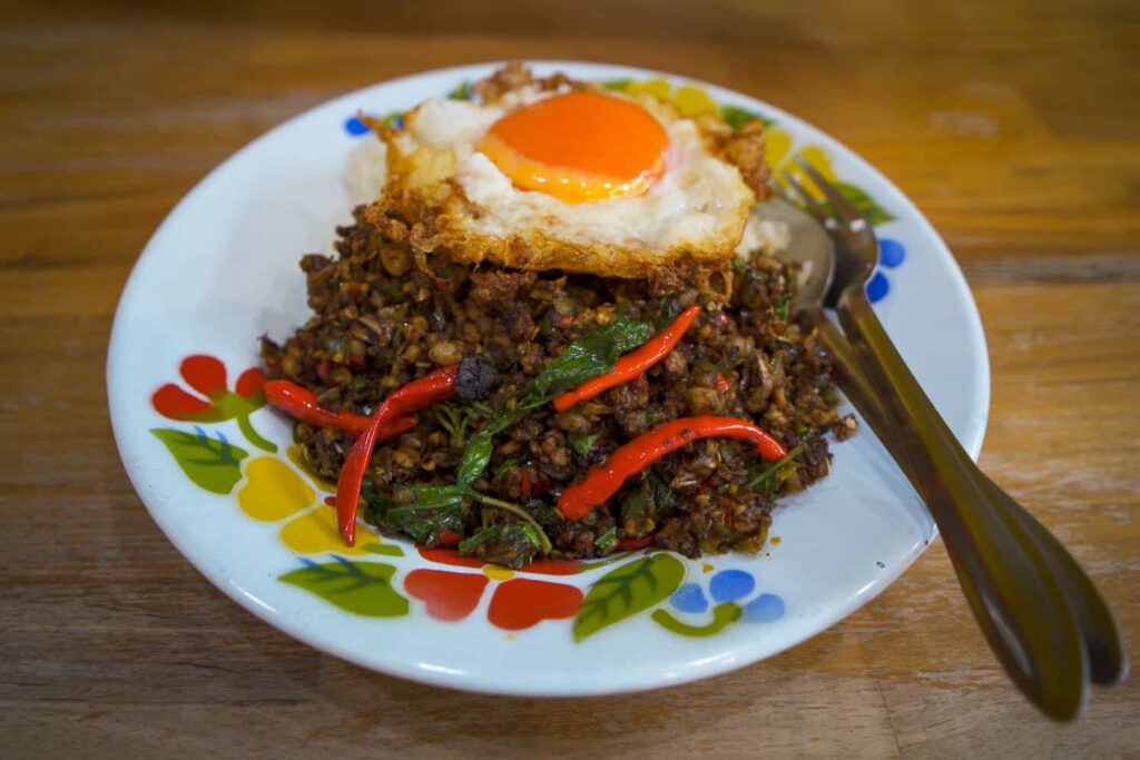 Plate of thai holy basil stir fry with fried duck egg on wooden table