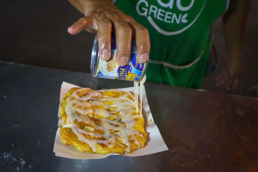 Hand pouring can of condensed milk onto thai roti pancake popular thai street food