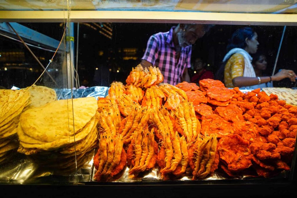 Sri Lankan food isso vade in glass case of vendor, man and woman standing behind