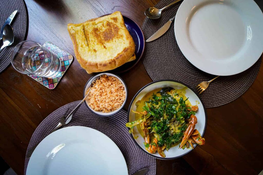 Bowl of Negombo Crab curry, coconut sombol, thick garlic toast on wooden table