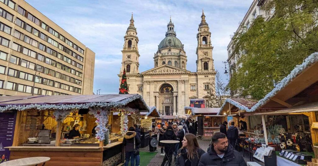 The imposing Basilica during the day, with wooden huts in the square in front decorated with lights and tinsel.