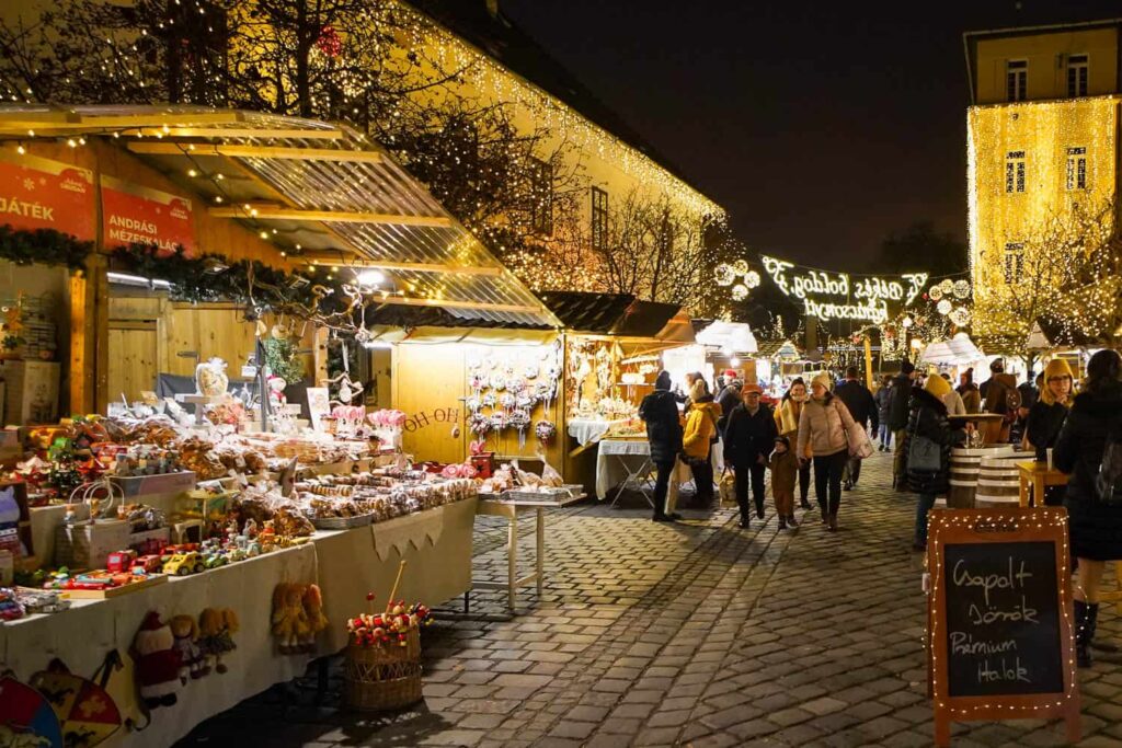 People walking down cobblestone street into Advent Obudan Christmas market surrounded by Christmas lights and wooden huts.