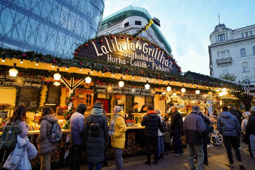 A long wooden hut with people inside selling Hungarian Christmas food, many people lined up in front at best Christmas market in Europe.