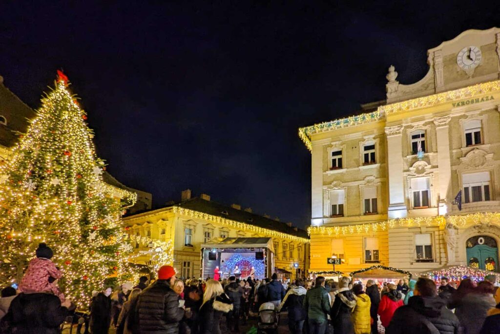 The square of the Advent Obudan Christmas market with tree adorned in lights, a stage with a band in the distance.