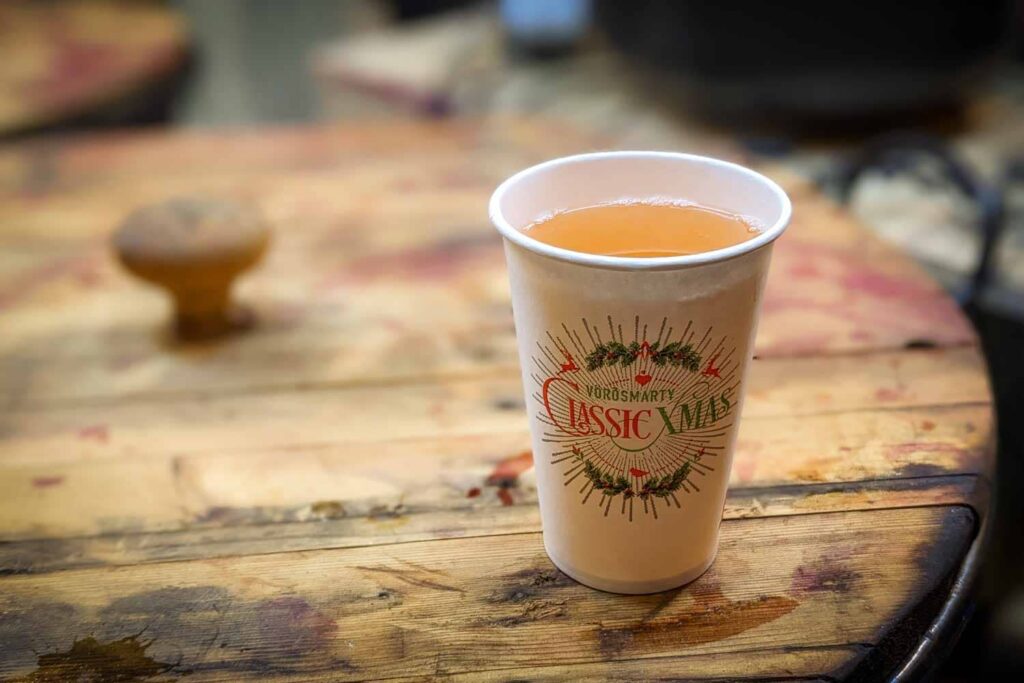 Colourful Christmas cup full of golden yellow mulled wine sitting on wooden barrel.