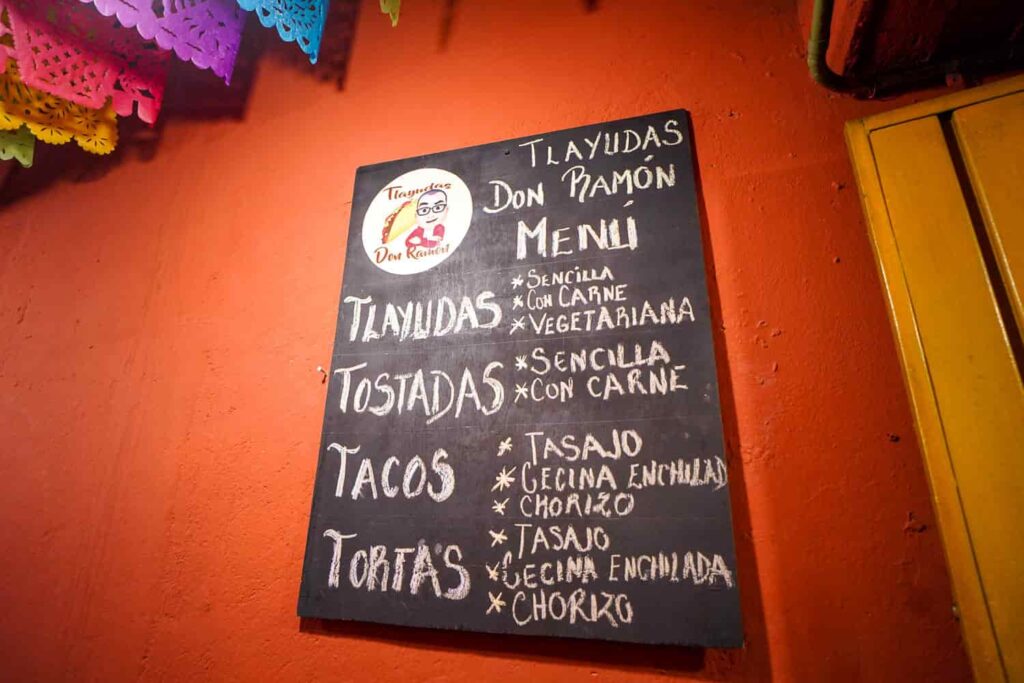Blackboard menu at Tlayudas Don Ramón, one of the best tlayuda spots in Oaxaca, hanging on a red wall.