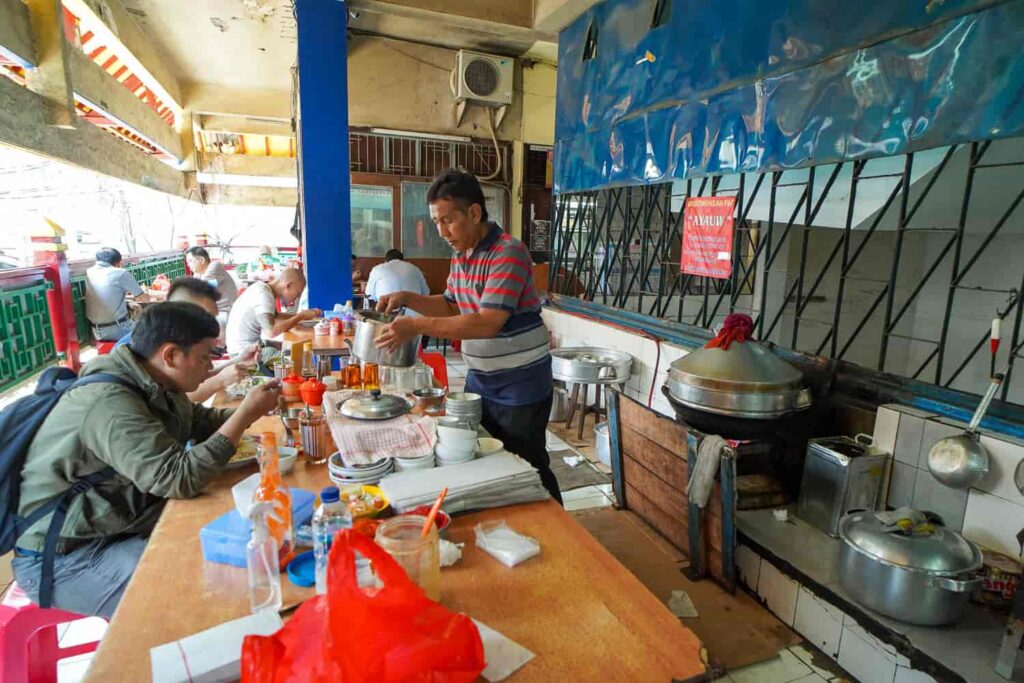 Man serving nasi tim chicken rice at a busy local eatery in Jakarta Chinatown