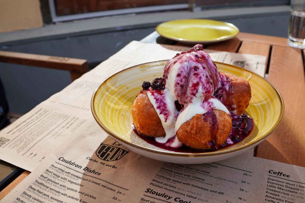 Romanian gogosi papanasi Brasov food covered in smântână and fruit compote in a yellow bowl on a rustic table