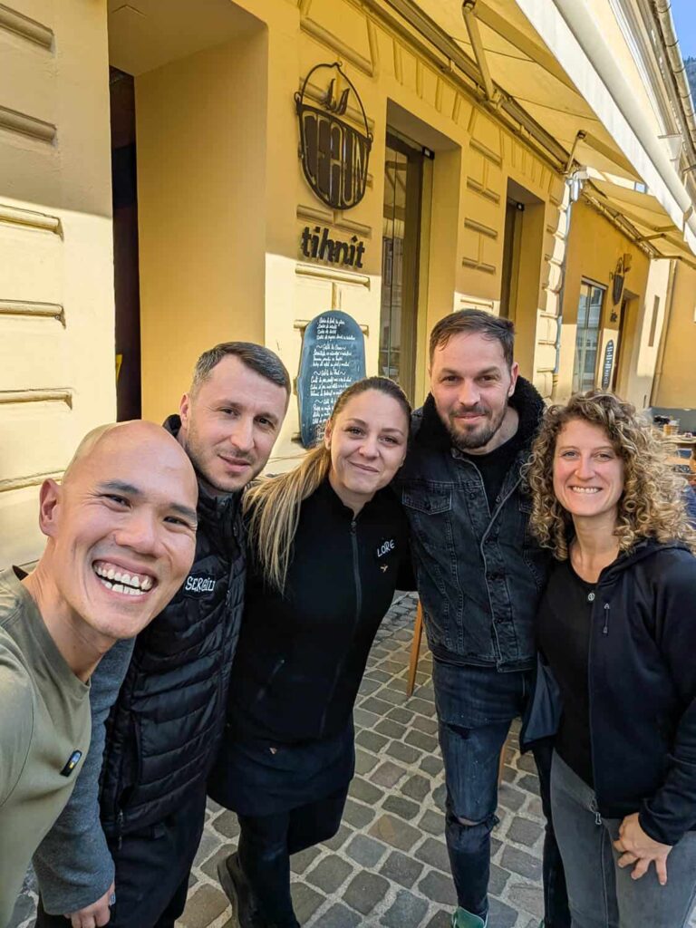 Hungry Two Travel in Brasov taking selfie with friendly locals in front of yellow La Ceaun restaurant