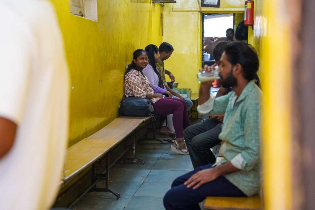 Customers sitting on benches in small lassi shop in Mumbai drinking the best lassi in Mumbai