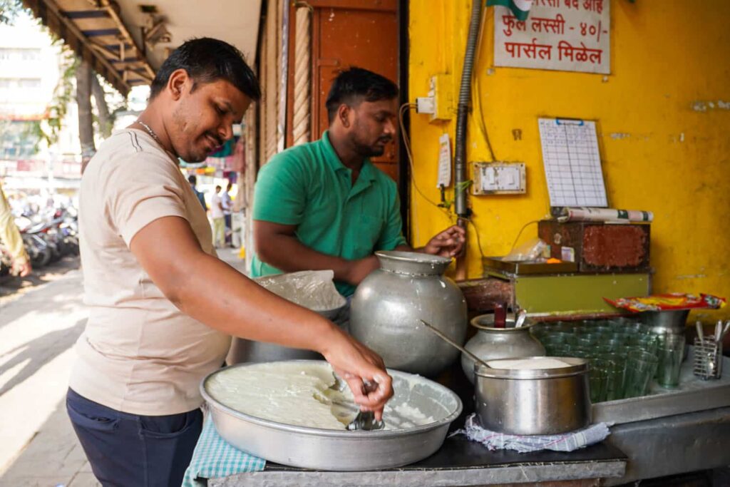 Two lassi makers standing at the front of a shop scooping thick creamy Indian yogurt