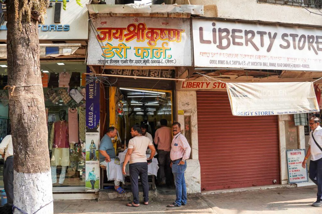 The front of Jai Shri Krishna Dairy Farm tiny lassi shop on busy street in Mumbai with Indian men standing out front