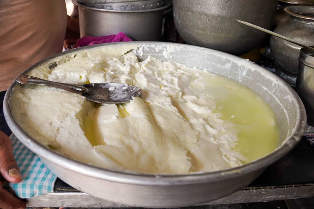 Metal circular tray of thick and creamy white yogurt with malai on top and scoop